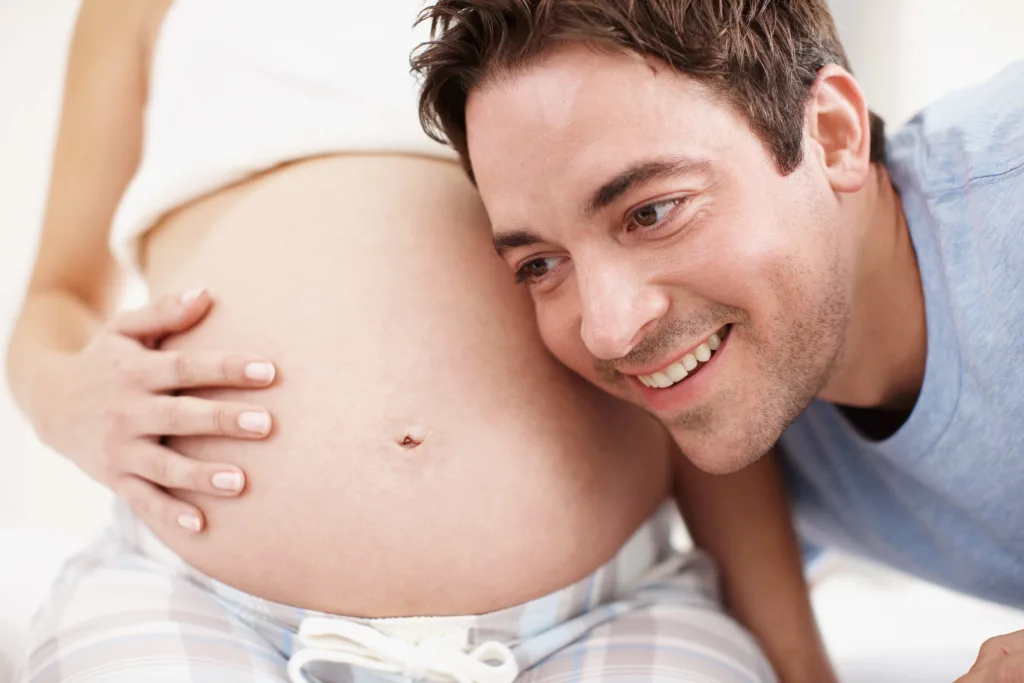 Mann legt seinen Kopf an den schwangeren Bauch der Frau